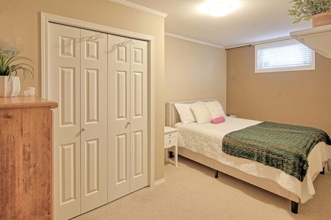 A bedroom with a bed, nightstand, and a plant.