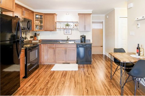 A kitchen with a black refrigerator and wooden floors.