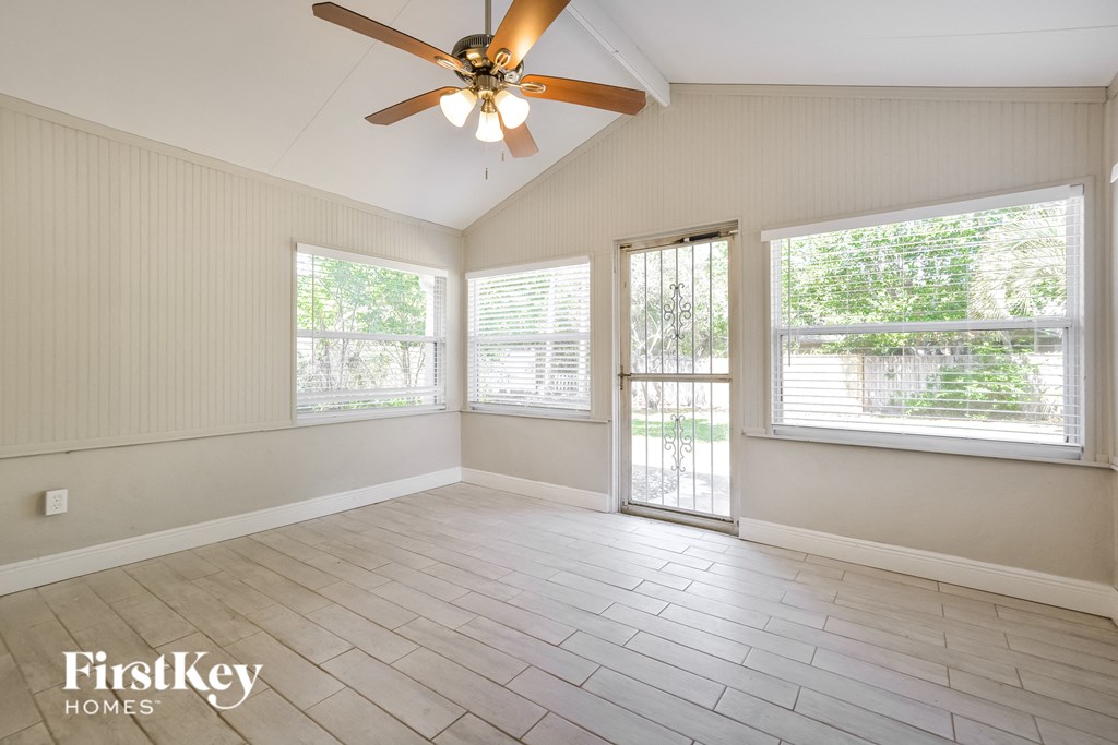 an empty living room with a ceiling fan and three windows