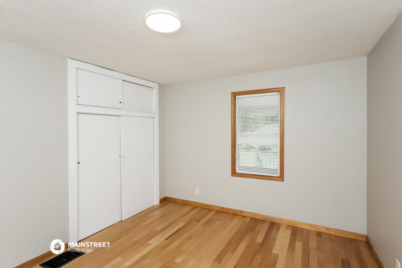 a living room with white walls and wood flooring and a window and a closet