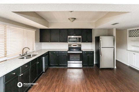 a kitchen with black cabinets and white appliances and a wooden floor