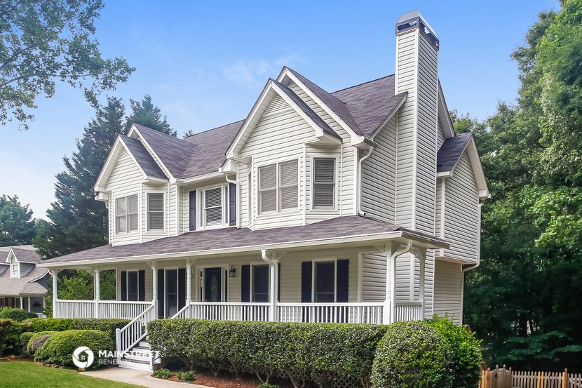 a white house with a large porch and a yard with bushes