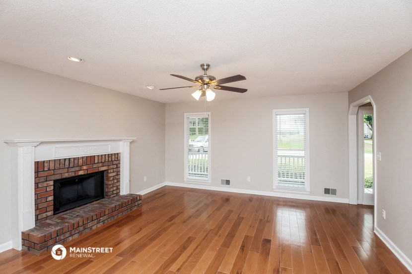 the living room with wood floors and a brick fireplace and a ceiling fan