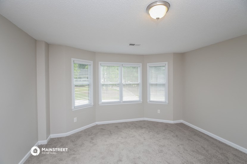 an empty living room with three windows and a carpet