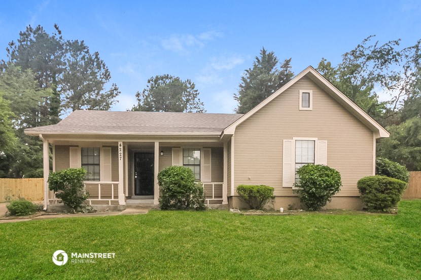 a small tan house with a green lawn and trees