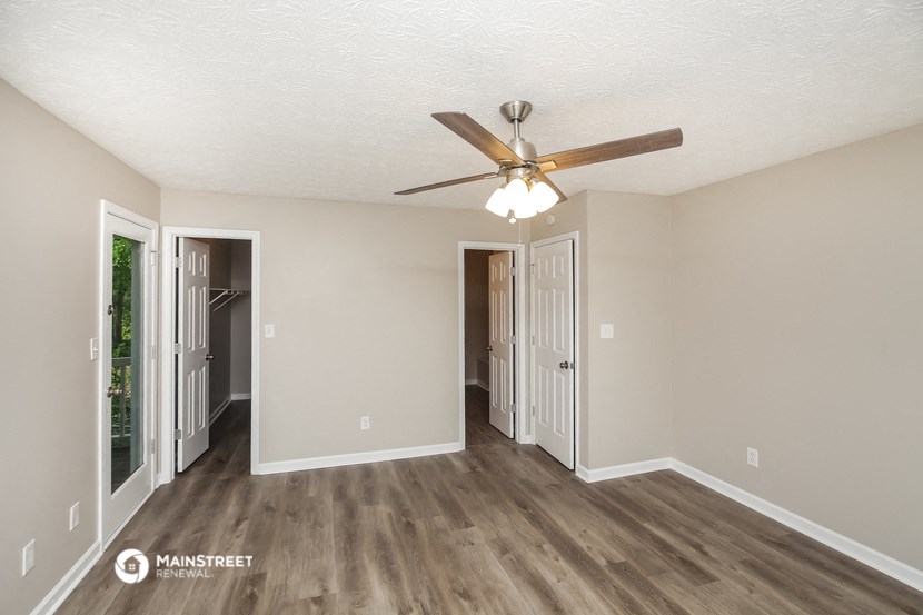 an empty living room with a ceiling fan and a door to a hallway