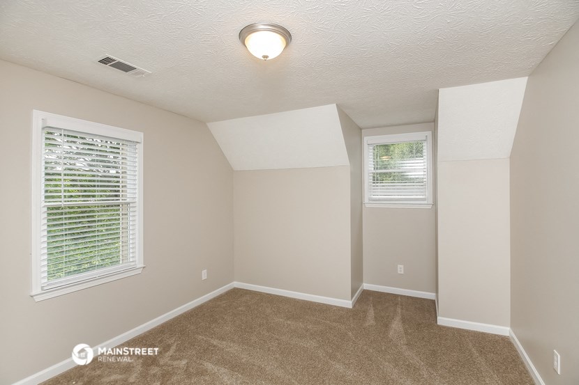 the spacious living room with carpeted flooring and two windows