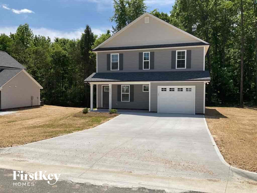 A two-story house with a garage is surrounded by trees and has a driveway leading to the front door.