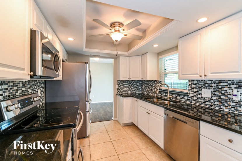 a kitchen with black counters and white cabinets and a ceiling fan
