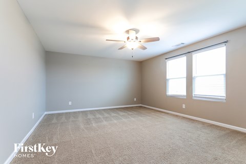 the spacious living room with ceiling fan and two windows