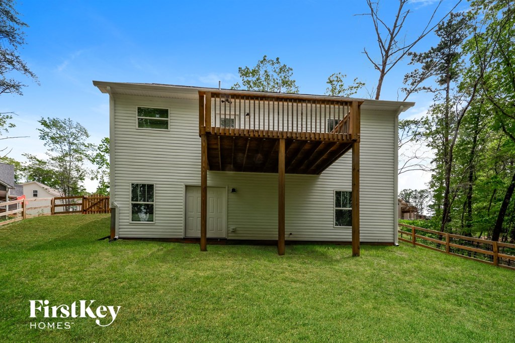 the back of a white house with a wooden deck on top of a yard
