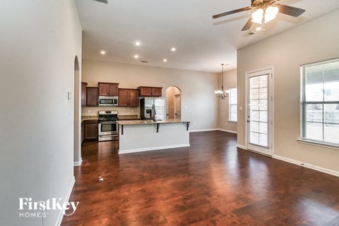 an empty living room with a kitchen and a ceiling fan