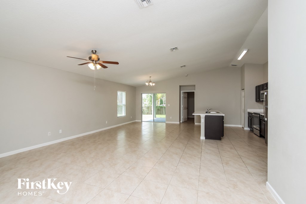 A spacious empty room with a ceiling fan and a door leading to another room.