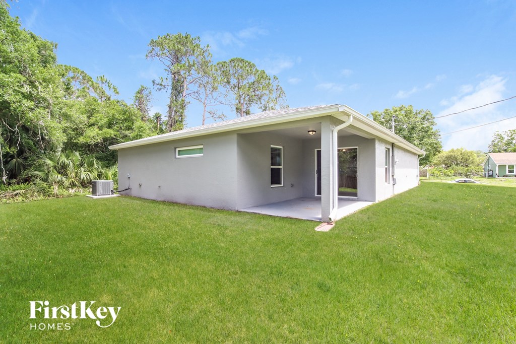 A small house with a white exterior is surrounded by green grass and trees.