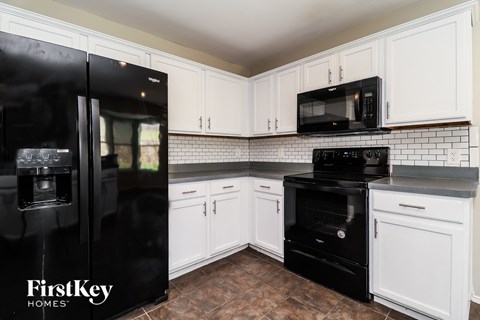 A black refrigerator is in a kitchen with white cabinets.