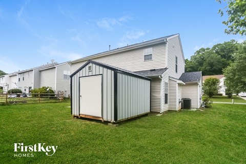 A metal shed is in the foreground of a grassy area in front of a house.