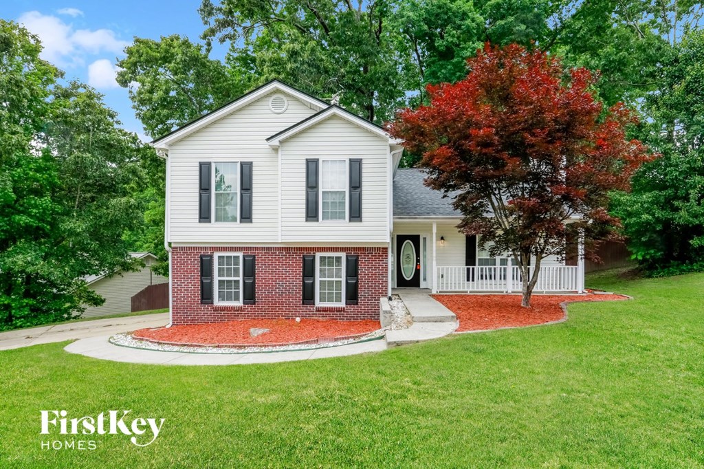 a white house with a red brick driveway and a tree