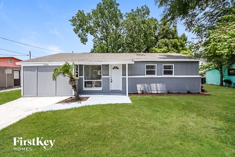 a gray house with a lawn and a palm tree