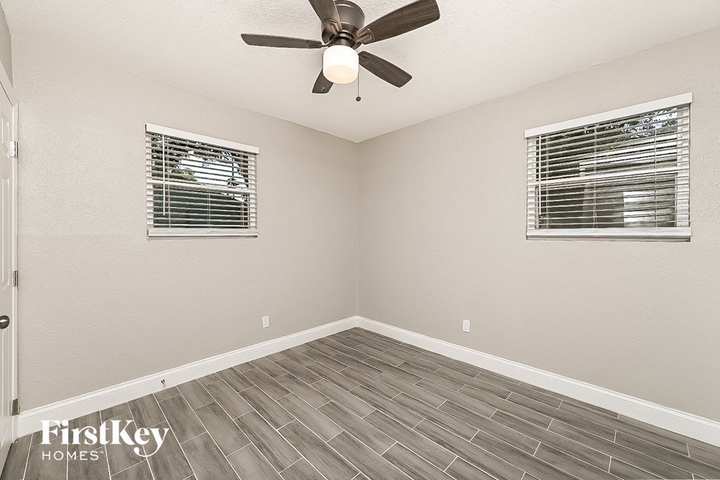 an empty room with a ceiling fan and two windows