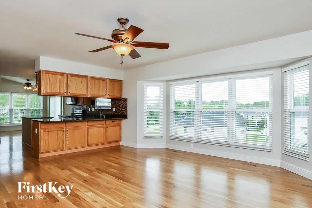 an empty living room with a ceiling fan and a kitchen