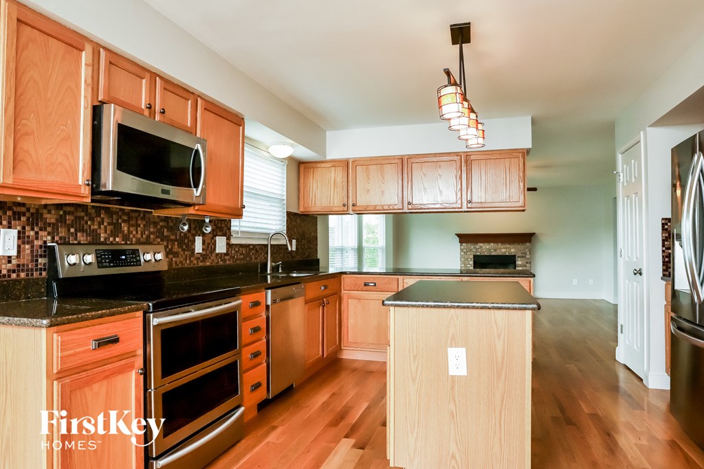 an updated kitchen with wood cabinets and black counter tops and stainless steel appliances