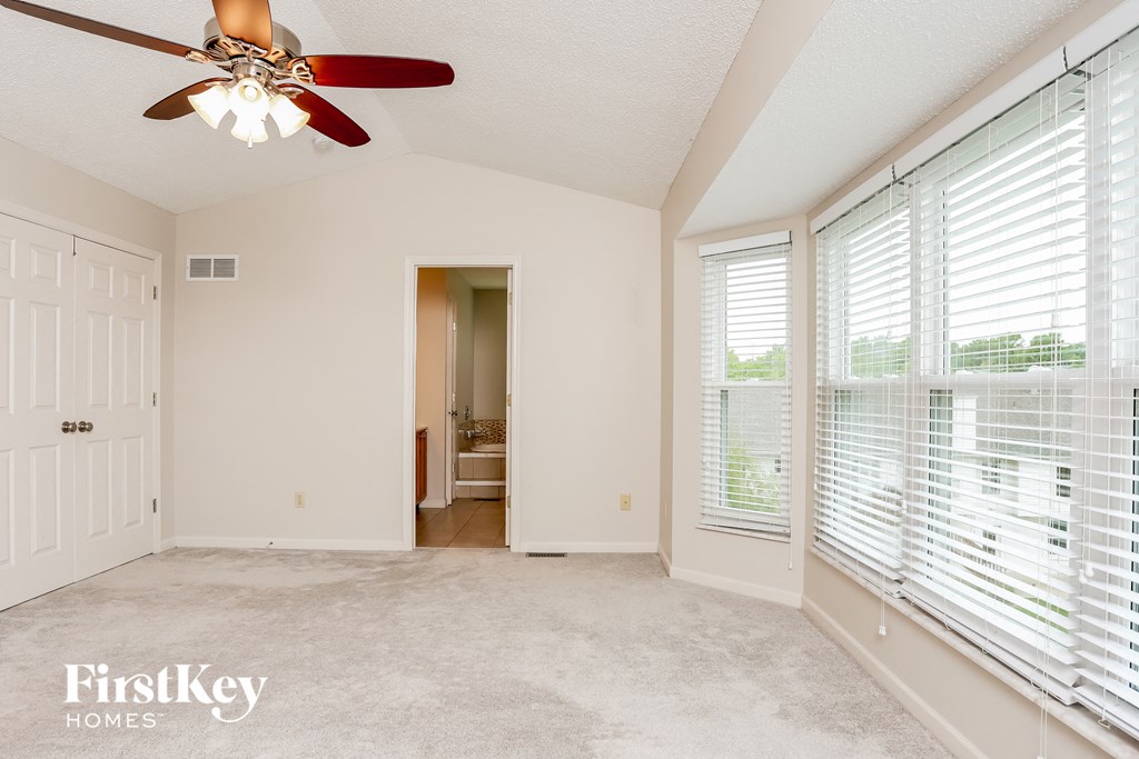 an empty living room with a ceiling fan and large windows