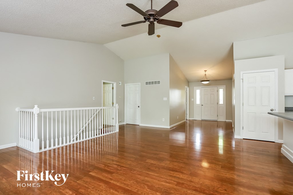 an empty living room with a ceiling fan and a staircase