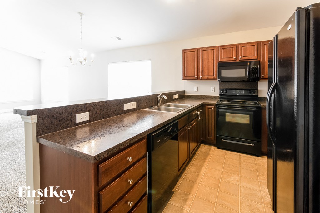 A kitchen with a black refrigerator and brown cabinets.