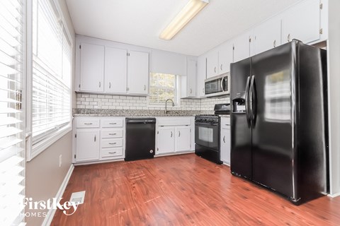 A kitchen with a black refrigerator and wooden floors.