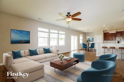 A living room with a beige couch, blue chairs, and a painting of a beach scene on the wall.