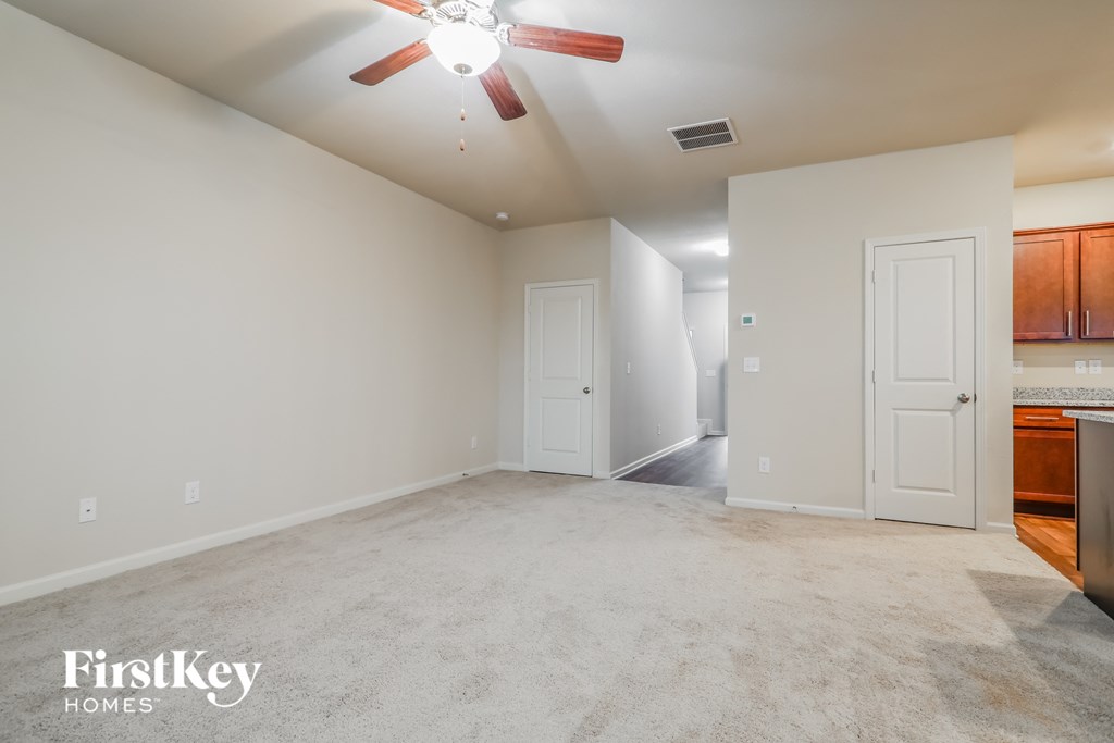 A spacious room with a ceiling fan and a kitchen area in the background.