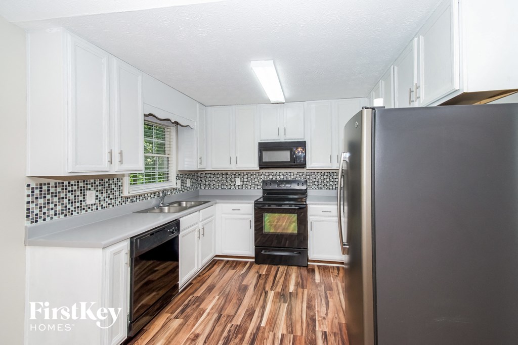 A kitchen with white cabinets and a black fridge.