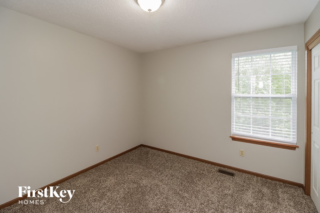 A room with a carpet floor, a window with blinds, and a door.