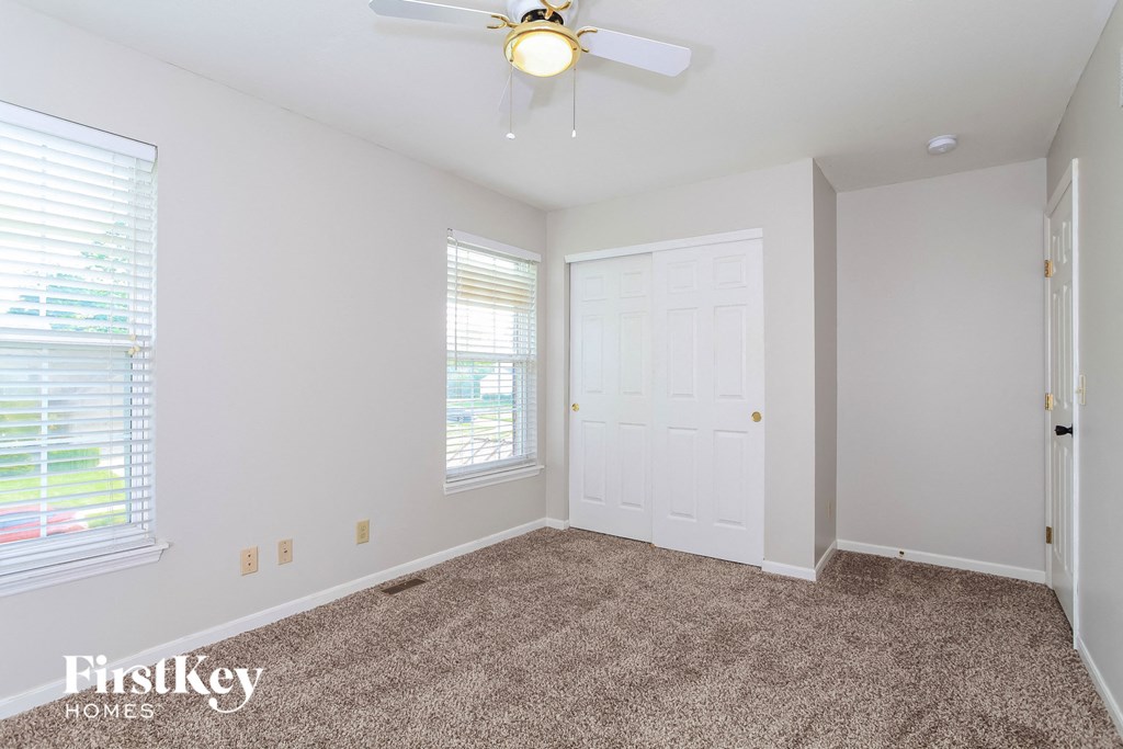 A room with a carpet floor, a ceiling fan, and a window with blinds.