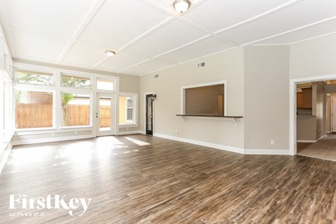 A spacious room with wooden flooring and white walls, featuring a large window and a door.