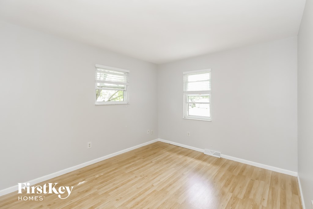 a bedroom with wood floors and white walls and two windows