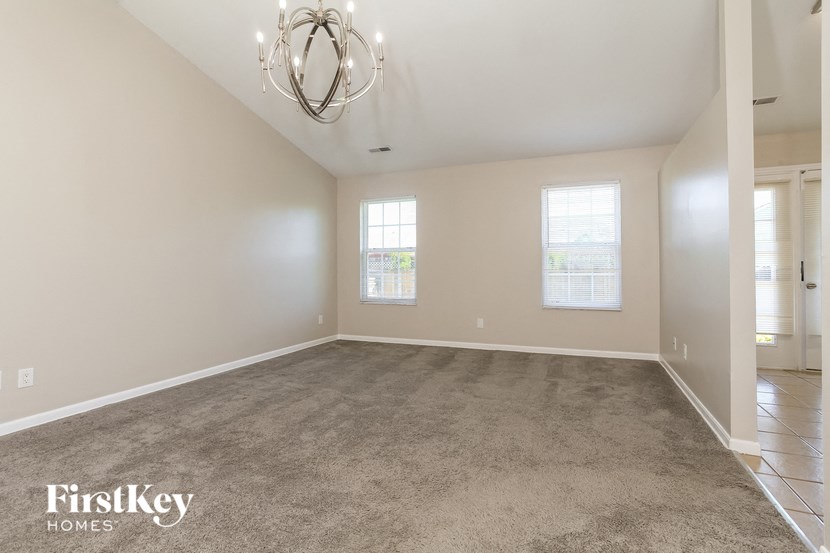 an empty living room with carpet and a chandelier