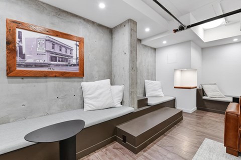 A room with a framed picture of a building on the wall and a bench with a cushion on it.