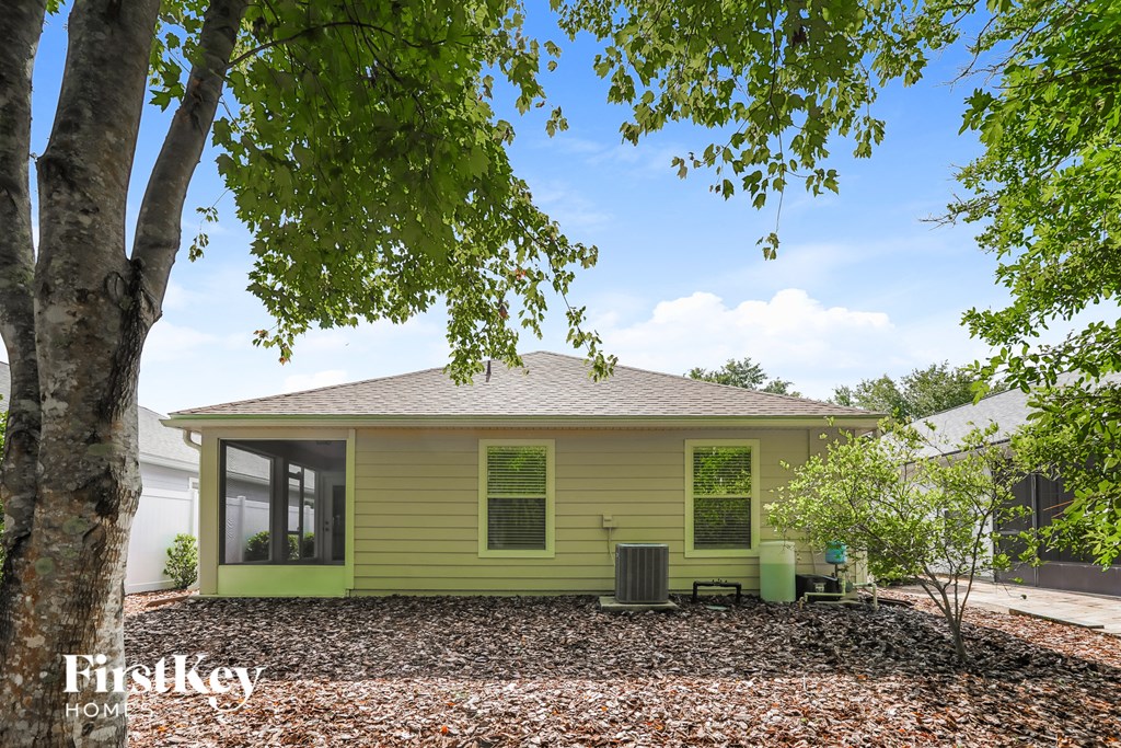 A small house with a green trim is surrounded by trees and has a gravel driveway.