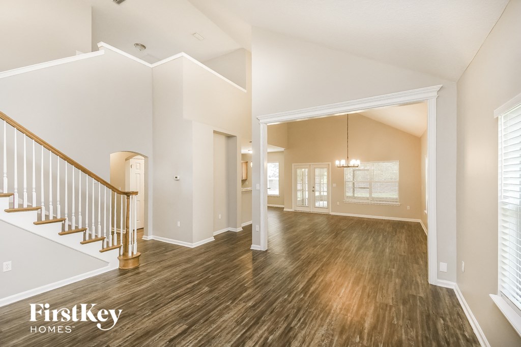 A spacious room with wooden floors and a staircase with a gold railing.