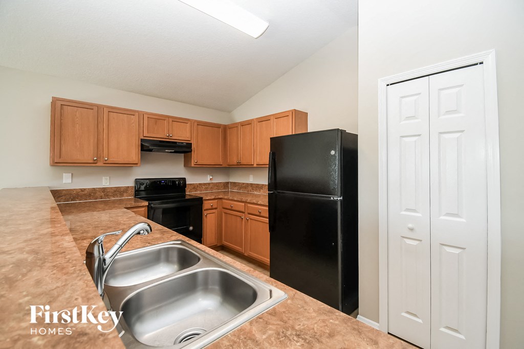 A kitchen with a black refrigerator and brown cabinets.