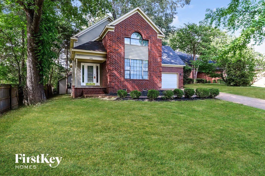 the front of a brick house with a lawn and trees