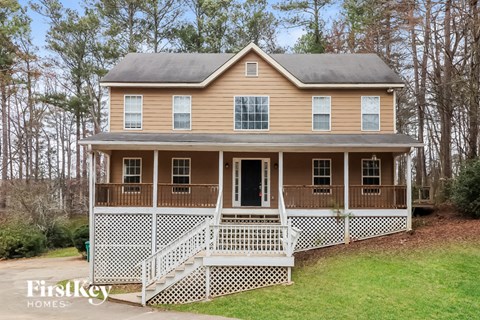 a tan house with a porch and a white fence