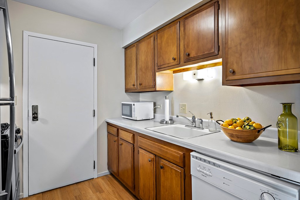 a kitchen with white appliances and wooden cabinets and a bowl of fruit on the counter