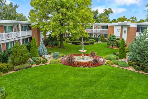 A courtyard with a fountain surrounded by trees and bushes.