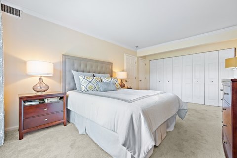 A bedroom with a large bed, a nightstand with a lamp, and a dresser with a mirror.