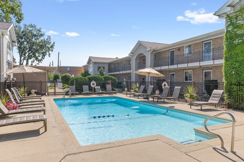 A swimming pool surrounded by lounge chairs and umbrellas in a residential area.