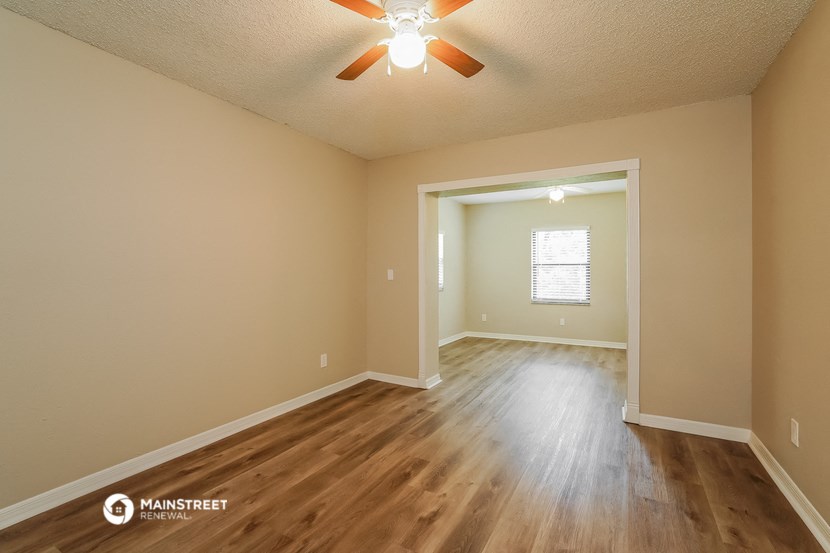 the spacious living room with hardwood flooring and a ceiling fan