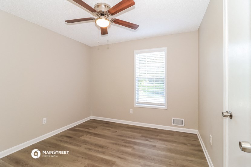 the spacious bedroom has a ceiling fan and hardwood flooring