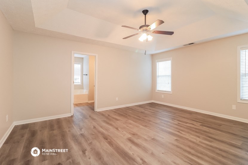 the spacious living room with hardwood flooring and a ceiling fan
